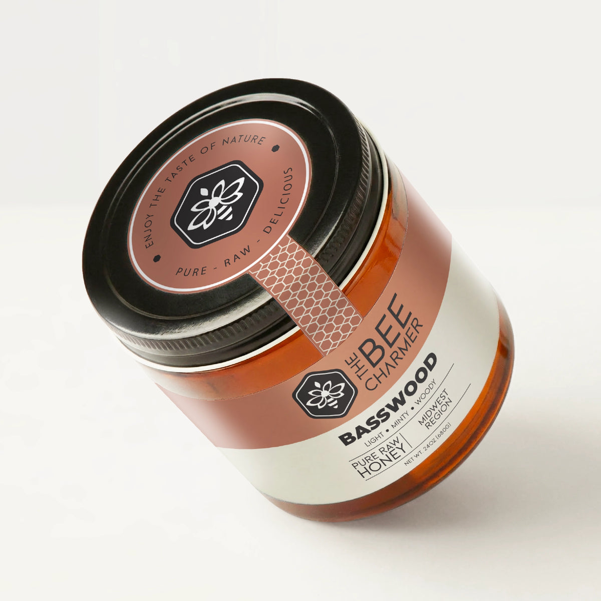 Pure raw Basswood Honey in a signature Bee Charmer branded 24oz wide-mouth glass jar showing the top of the jar label.
