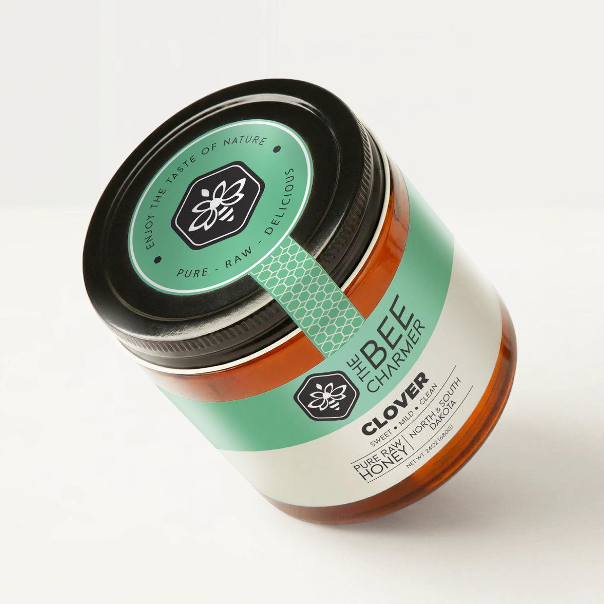 Pure raw Clover Honey in a signature Bee Charmer branded 24oz wide-mouth glass jar showing the top of the jar label.