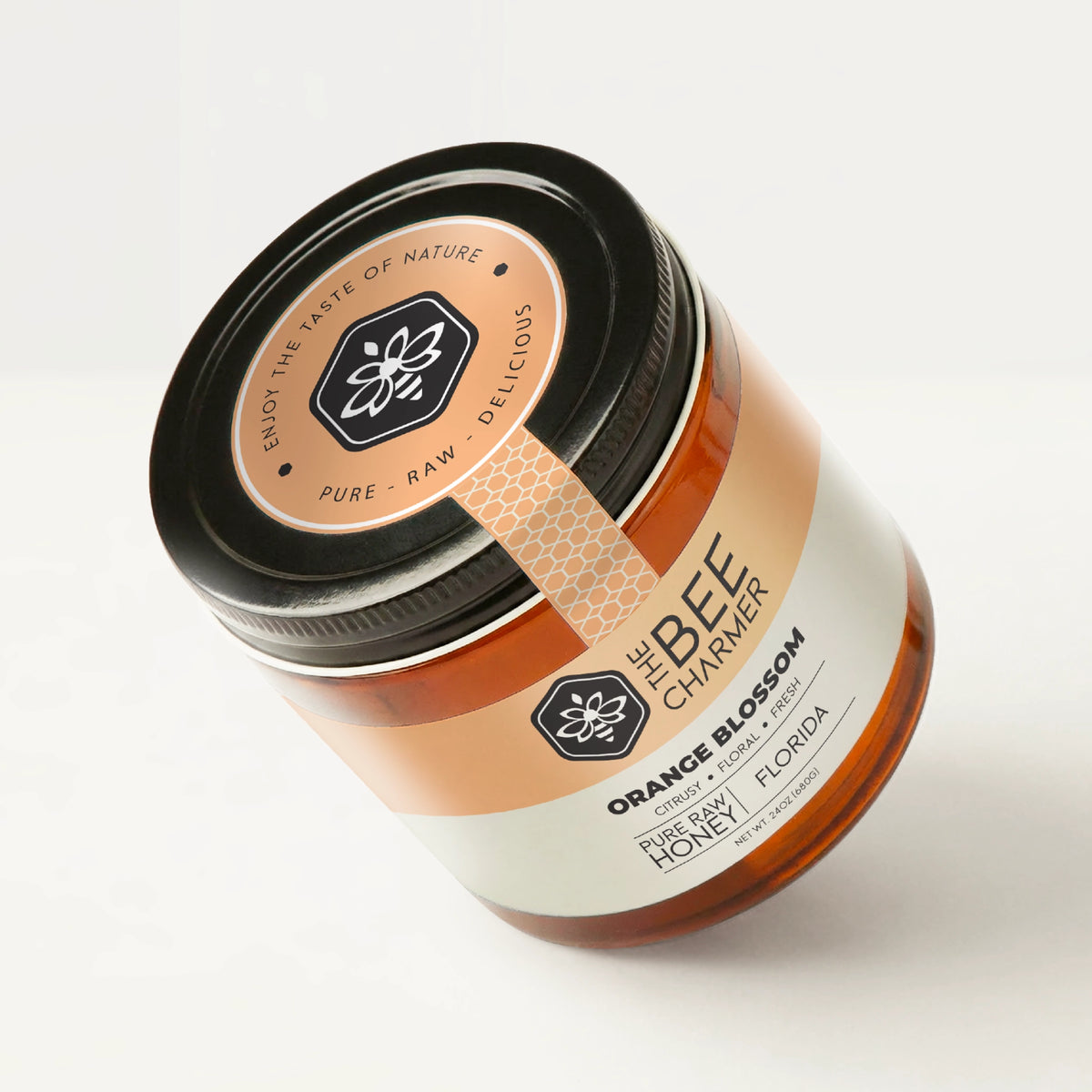 Pure raw Orange Blossom honey in a signature Bee Charmer branded 24oz wide-mouth glass jar showing the top of the jar label.