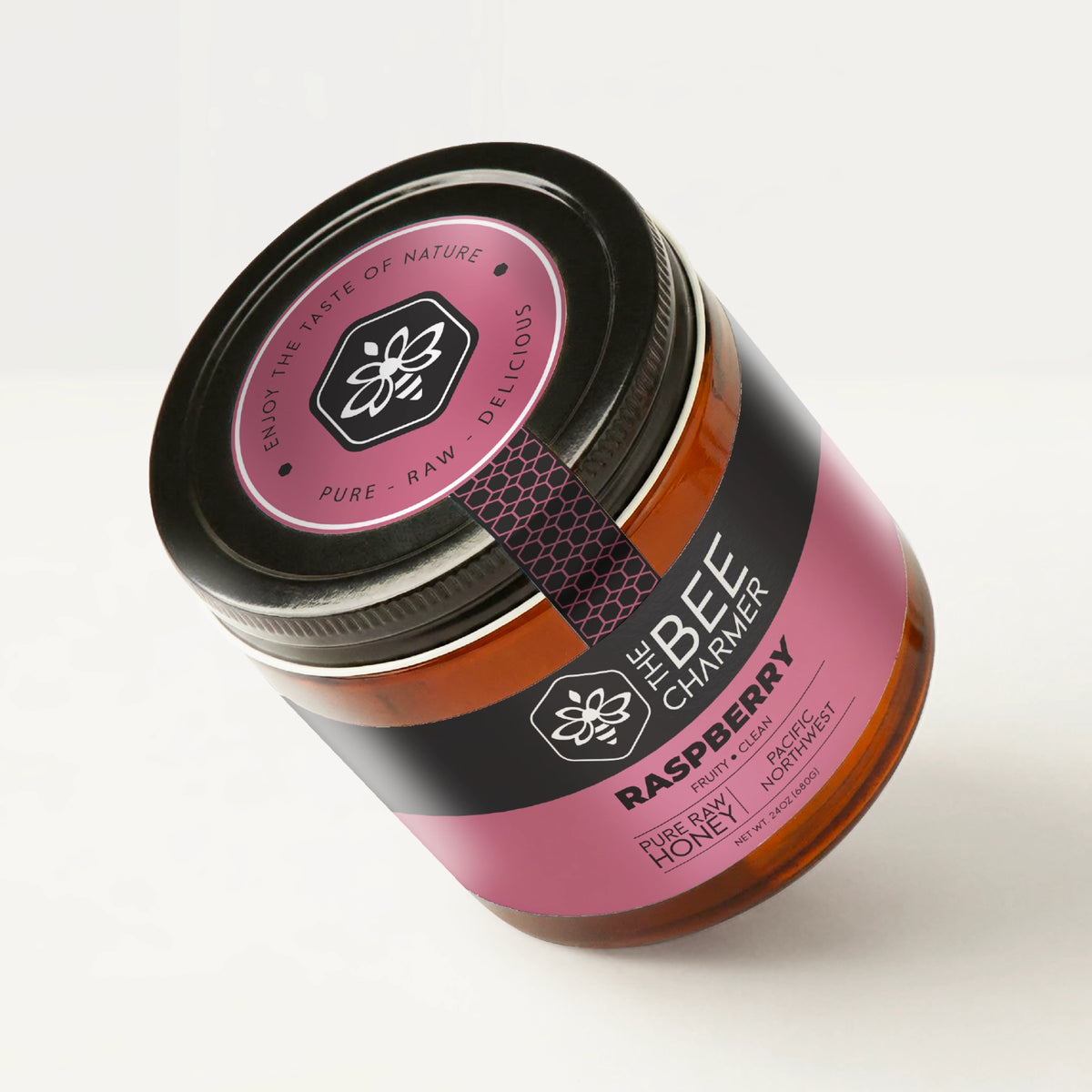 Pure raw Raspberry honey in a signature Bee Charmer branded 24oz wide-mouth glass jar showing the top of the jar label.