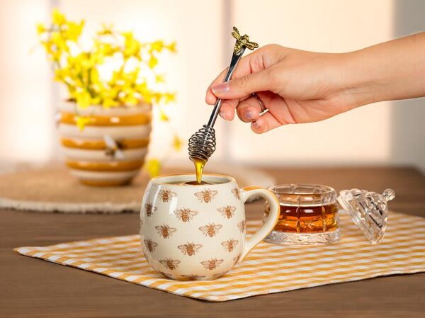 A Honey Dauber with a bee handle design drizzling honey into a cup  of tea.
