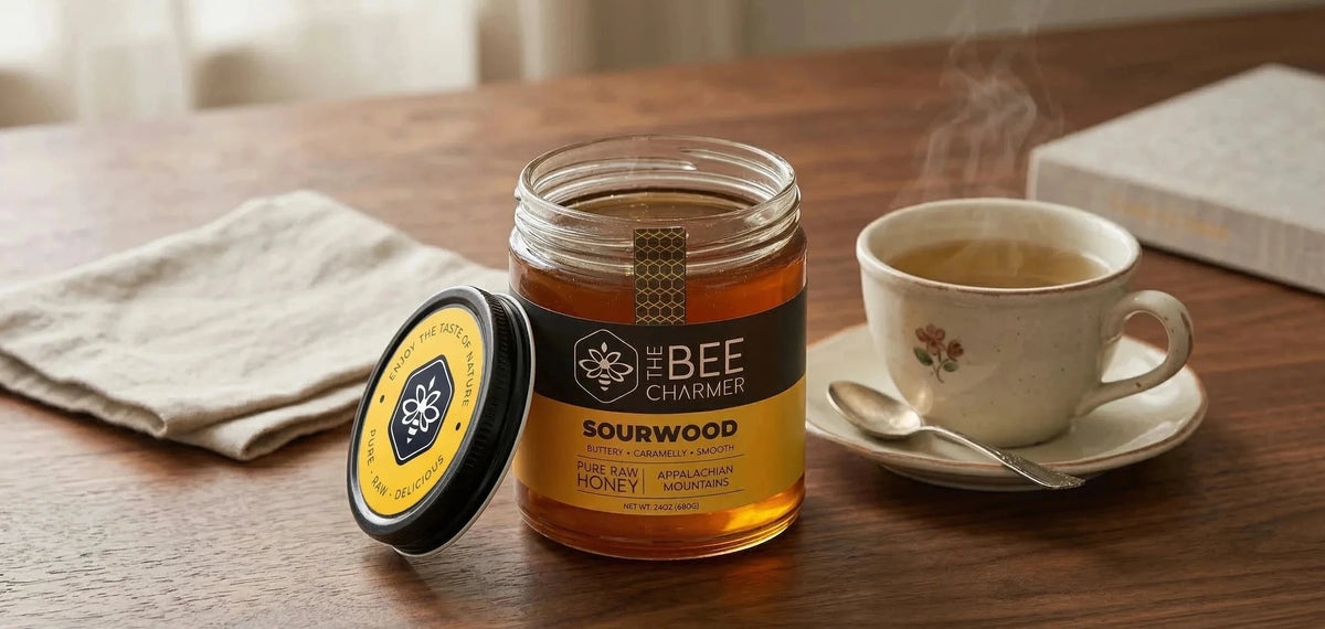 A 24oz jar of Sourwood honey from The Bee Charmer on a wooden table with a cup of tea.